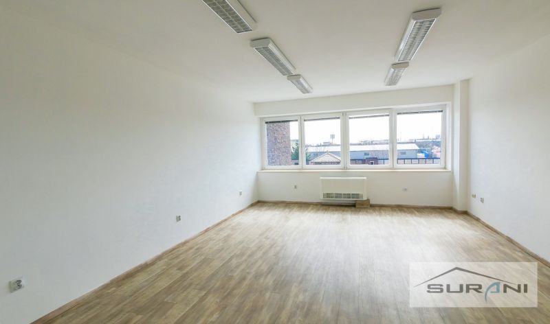 An office with white walls and a wooden decor floor, large windows as a source of light.