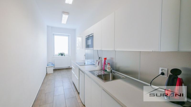 Office kitchen with light furniture and appliances, with a wood-patterned floor.