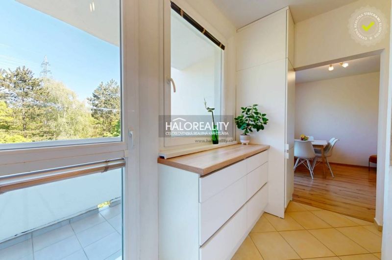 A kitchen in a 3-room apartment with white furniture and a view of the surroundings.