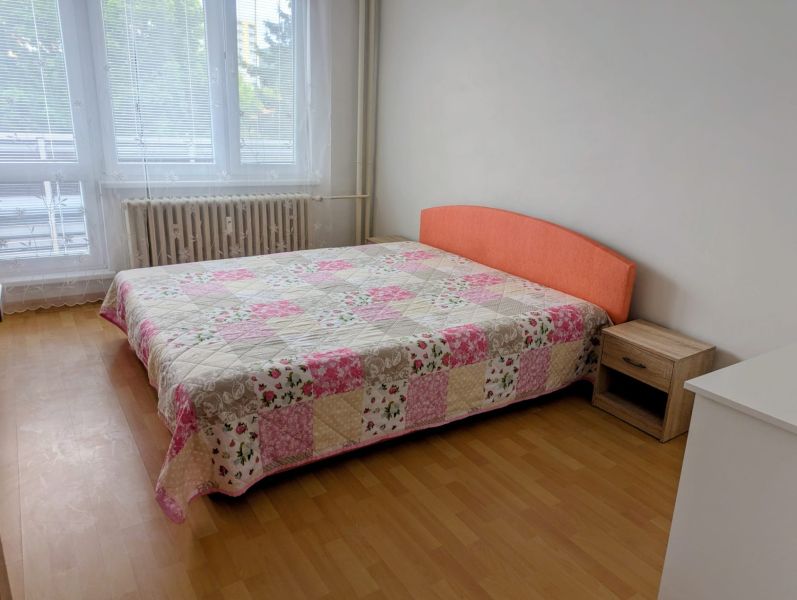 Bedroom with a bed and a patchwork bedspread in a 2-room apartment, floor with a wooden decor.