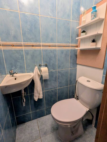 A bathroom with blue tiles and a toilet in a 2-room apartment, shelves on the wall.