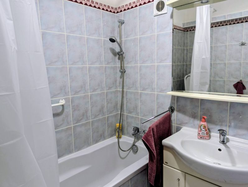 Bathroom in a 2-room apartment with a bathtub, sink, and ceramic tiles.