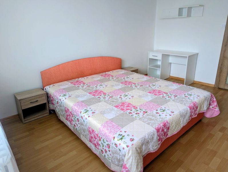 Bedroom in a 2-room apartment with a bed, a desk, and a wooden decor floor.