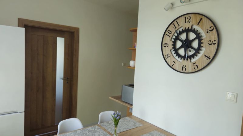 Interior of a 2-room apartment with a clock on the wall, wooden doors, and a table.