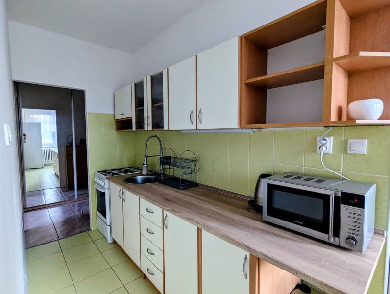 A kitchen in a 2-room apartment with a microwave and a stovetop, leading into another room.