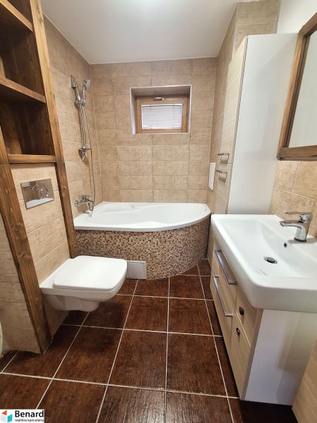 A bathroom in a 2-room apartment with a bathtub and cabinets, light brown tiles and flooring.