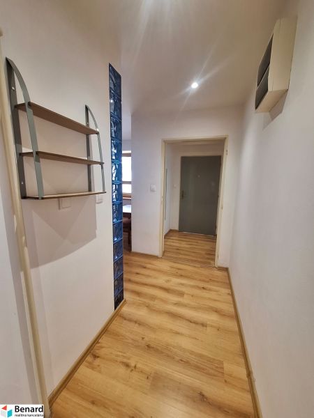A hallway in a 2-room apartment with a wooden floor and a shelf on the wall.