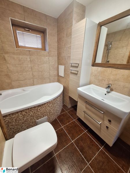 A bathroom with a corner bathtub, sink, and toilet in a 2-room apartment.