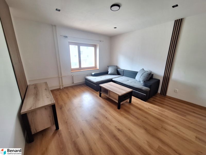 Living room in a 2-room apartment with a sofa, tables, and wooden flooring.