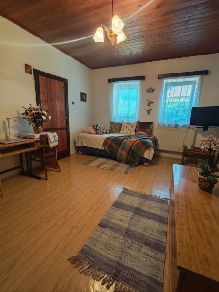 A room with a sofa, wooden decor flooring, flowers, and a table in a family house.