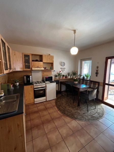 A kitchen in a family house with wooden cabinets and a dining table surrounded by plants.