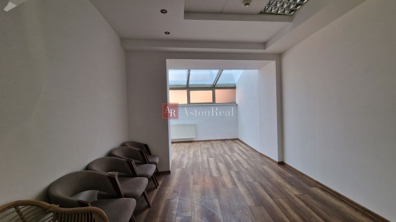 Interior of commercial premises with wood-patterned flooring and chairs by the wall.