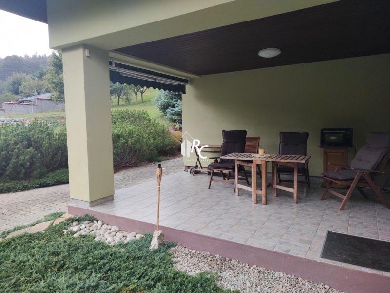 The terrace of a family house in Trebostovo with wooden garden furniture and landscaped greenery.
