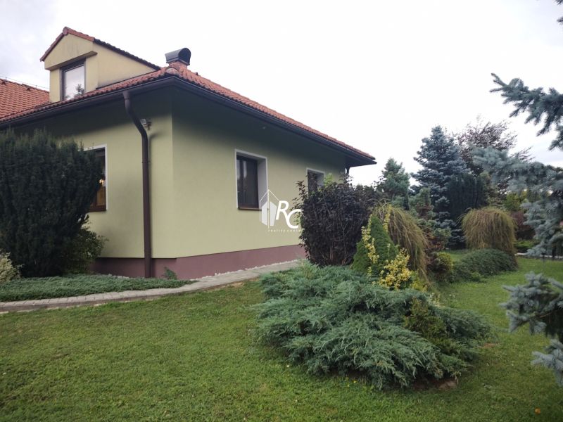 A family house in Trebostovo with a landscaped garden and wooden roof details.