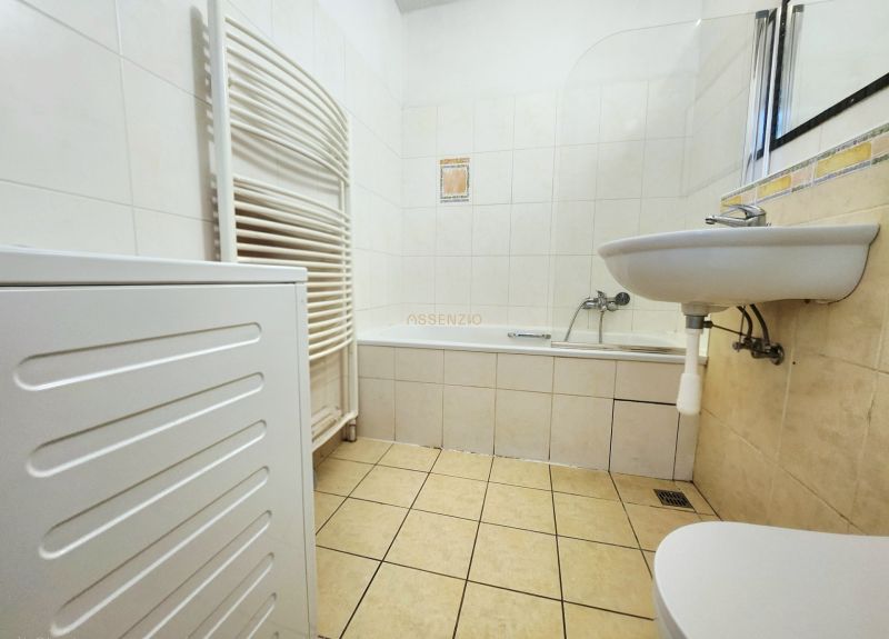 A bathroom in a 2-room apartment with a bathtub, sink, and washing machine, tiled with white tiles.