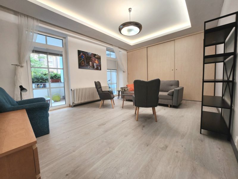 Living room in a two-room apartment, wooden decor flooring, furniture, large windows.