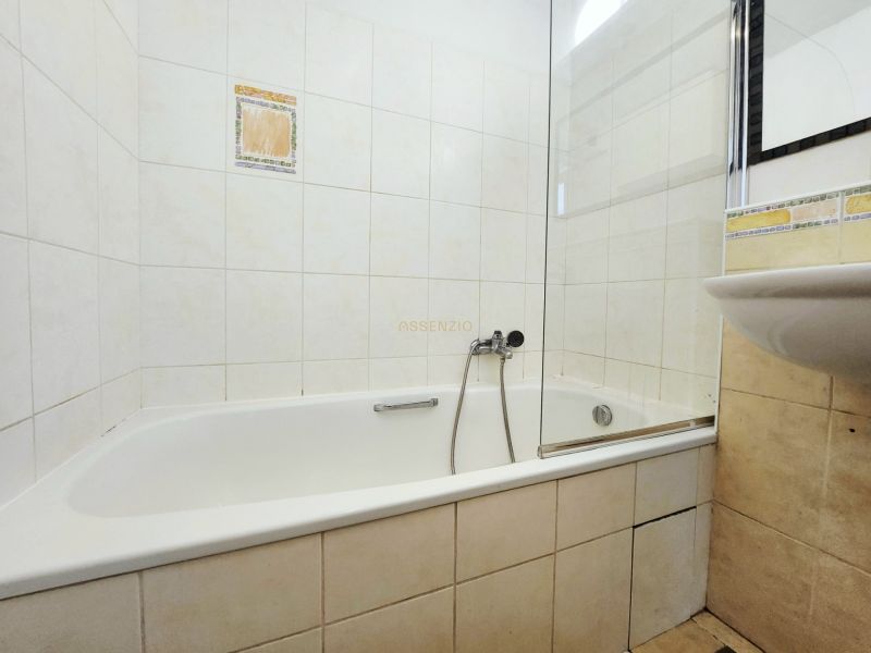 Bathroom in a 2-room apartment with a bathtub and a sink, tiled with light tiles.
