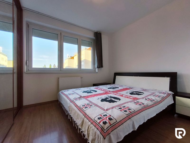 Bedroom in a 2-room apartment with wood-patterned flooring and a large window.