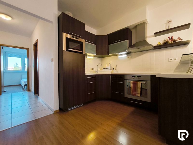 The kitchen of a two-room apartment with dark furniture and a wooden decor floor.