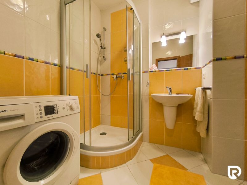 A bathroom with a washing machine, shower, and yellow tiles in a 2-room apartment.