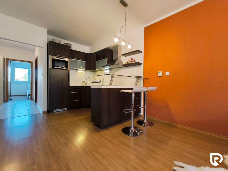 A kitchen in a 2-room apartment with a striking orange wall and a floor with a wood decor.