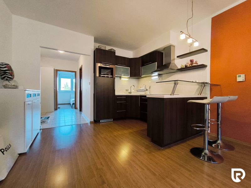 A kitchen in a 2-room apartment with a wooden decor floor and an orange wall.