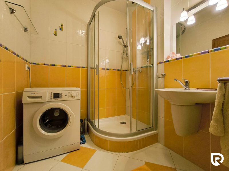 Bathroom in a 2-room apartment with a washing machine, shower corner, and yellow tiles.