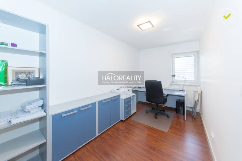 A study with an office desk, chair, and shelf in a family house, with a wooden-patterned floor.