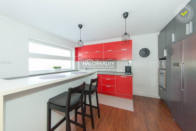 A kitchen in a family house with a red kitchen unit, a bar counter, and a floor with a wooden decor.