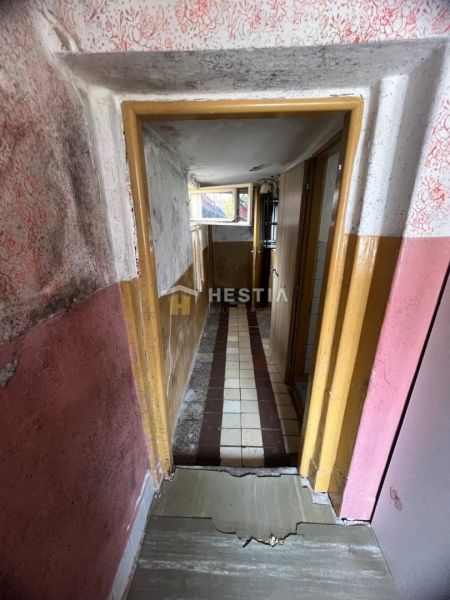 A narrow hallway with damaged walls and a tiled floor in a family house.