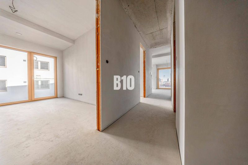 A hallway in a 3-room apartment with large windows and a concrete floor.
