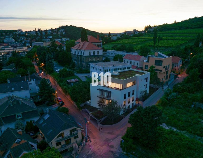 The building on Pod Strážami in Bratislava III surrounded by greenery and residential houses.