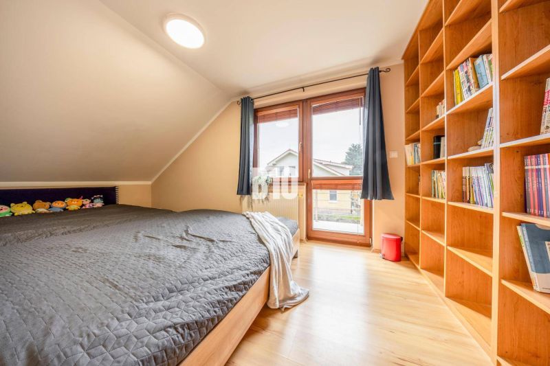Attic room with a bed, bookshelf, and wooden decor flooring in a family house.