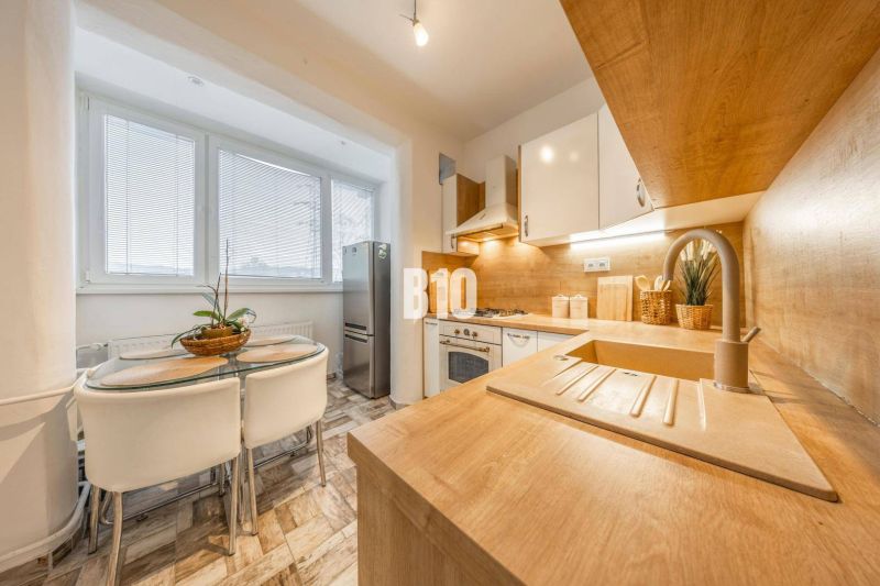 A kitchen in a 2-room apartment with a wooden decor floor and a dining area.