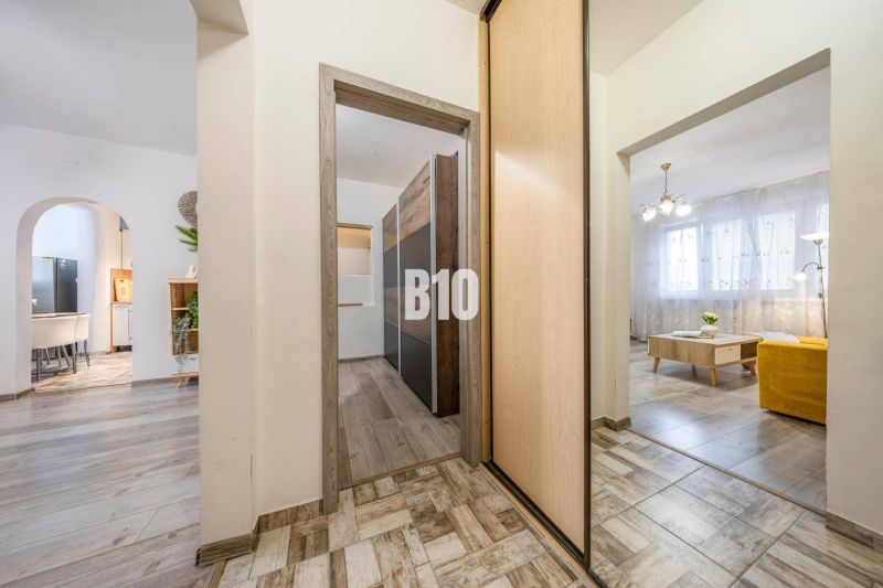 Interior of a 2-room apartment with a wooden decor floor, light furniture, and arched transitions.