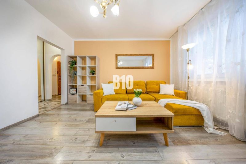 A living room in a two-room apartment with a yellow sofa and a floor with a wooden decor.