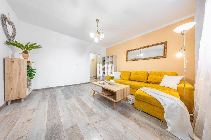 A living room in a two-room apartment with a wooden decor floor and a yellow sofa.