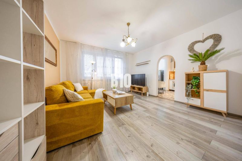Living room in a two-room apartment with a yellow sofa and a wooden decor floor.