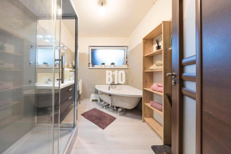 A bathroom in a family house with a bathtub, shower, and furniture with a wooden decor.