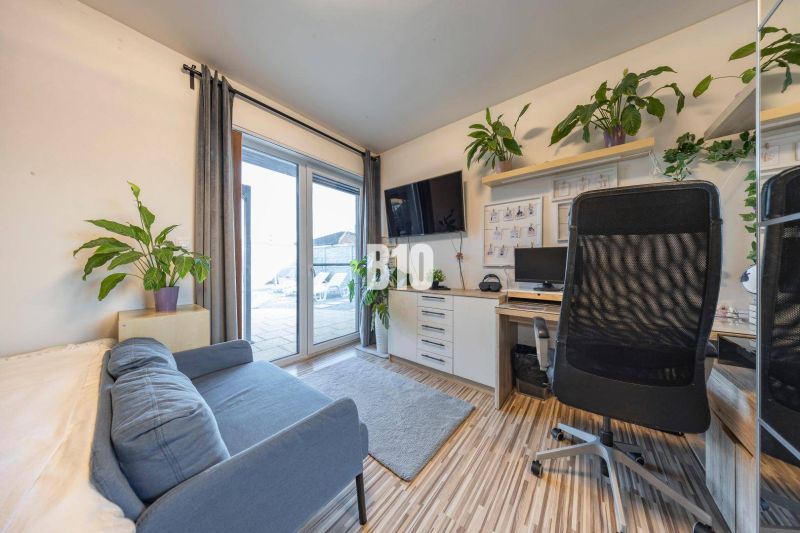 Office in a family house with a sofa, desk, television, and plants.