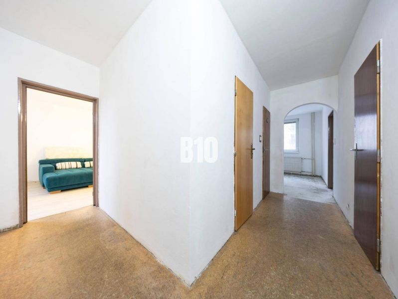A hallway in a 4-room apartment with a view of a room with a couch, floor with a wood decor.