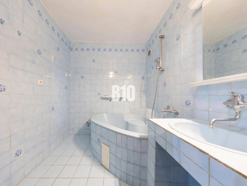 A bathroom with light blue tiles, a bathtub, and a sink in a 4-room apartment.