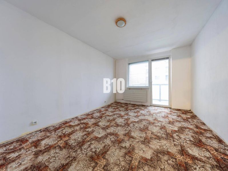 Living room in a 4-bedroom apartment with carpeted flooring and a large window.