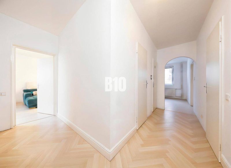 A hallway in a 4-room apartment with a wooden decor floor and light-colored walls.