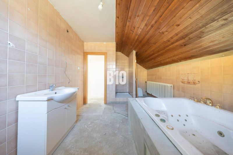 A bathroom in a family house with a bathtub, tiles, and a wooden ceiling.
