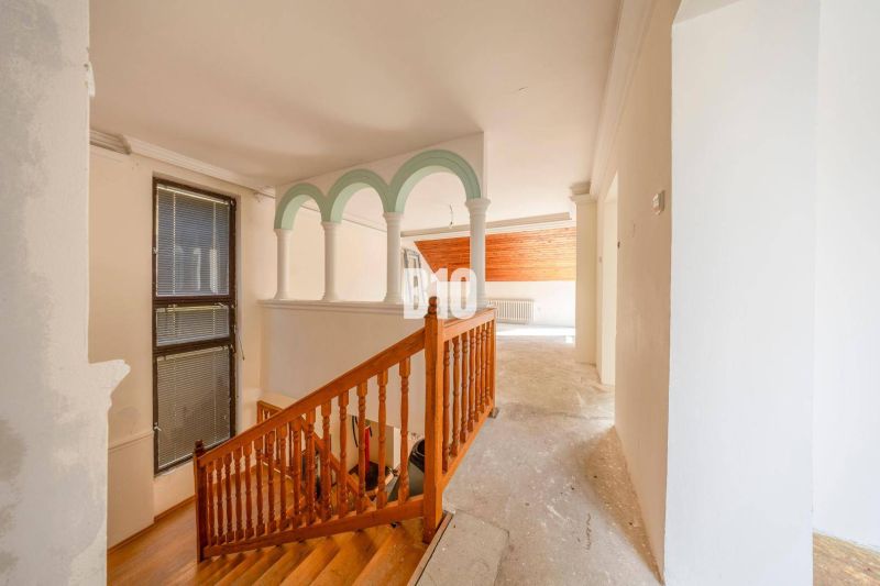 Interior of a family house with a wooden staircase and arched columns.