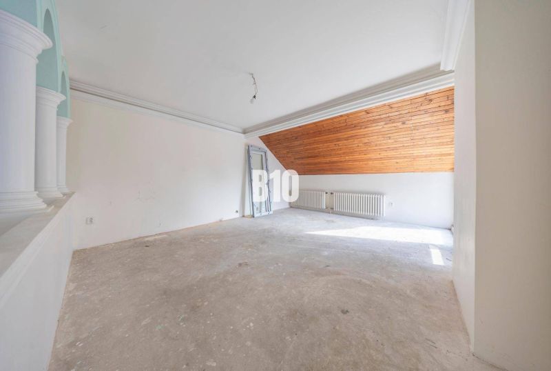 An unfurnished room with a radiator and a wooden ceiling in the attic of a family house.