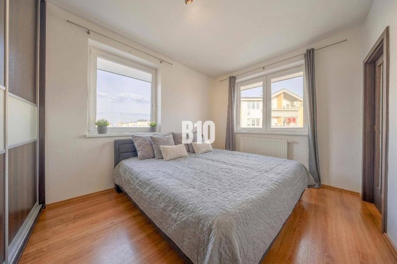 A bright bedroom with a bed, large windows, and a wooden decor floor in a two-room apartment.