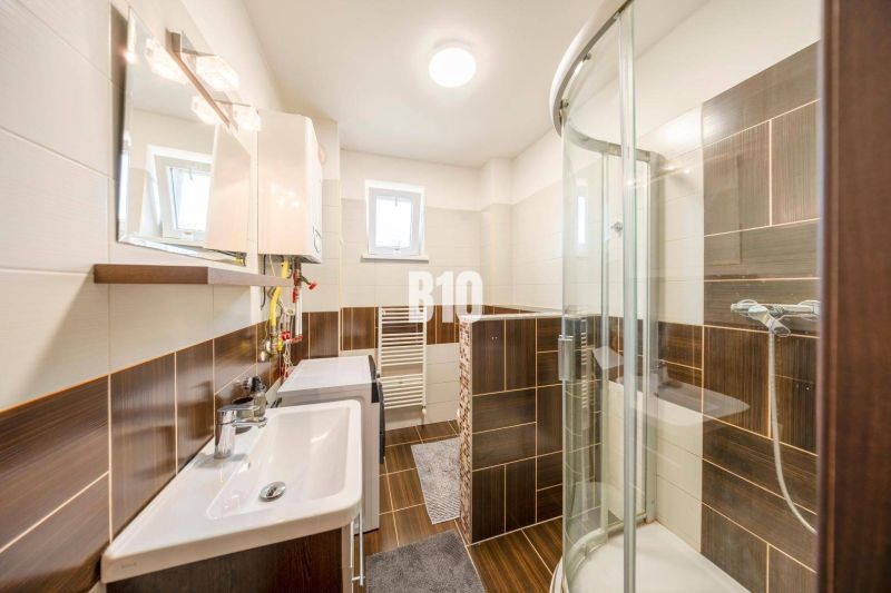 A bathroom in a 2-room apartment with dark tiles and a shower corner.