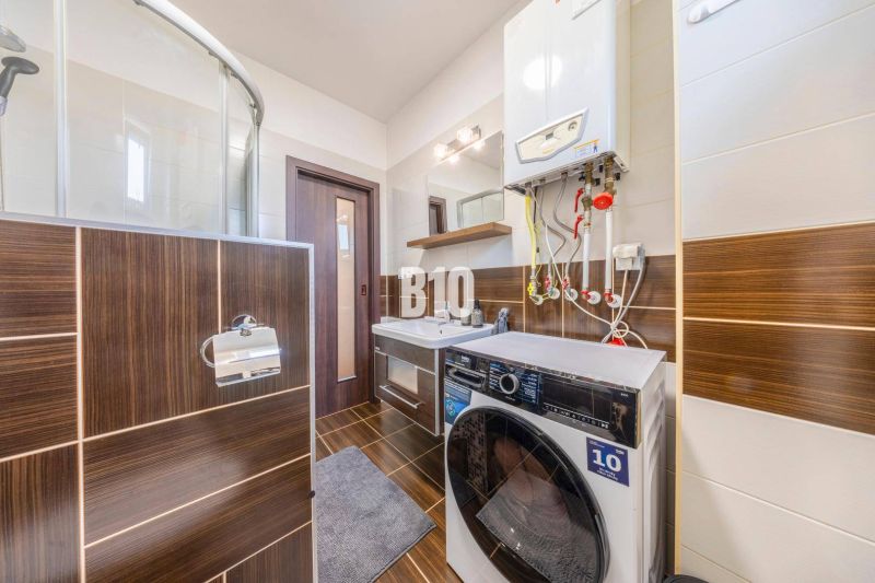 Bathroom with a washing machine and a shower in a 2-room apartment with a wooden decor floor.
